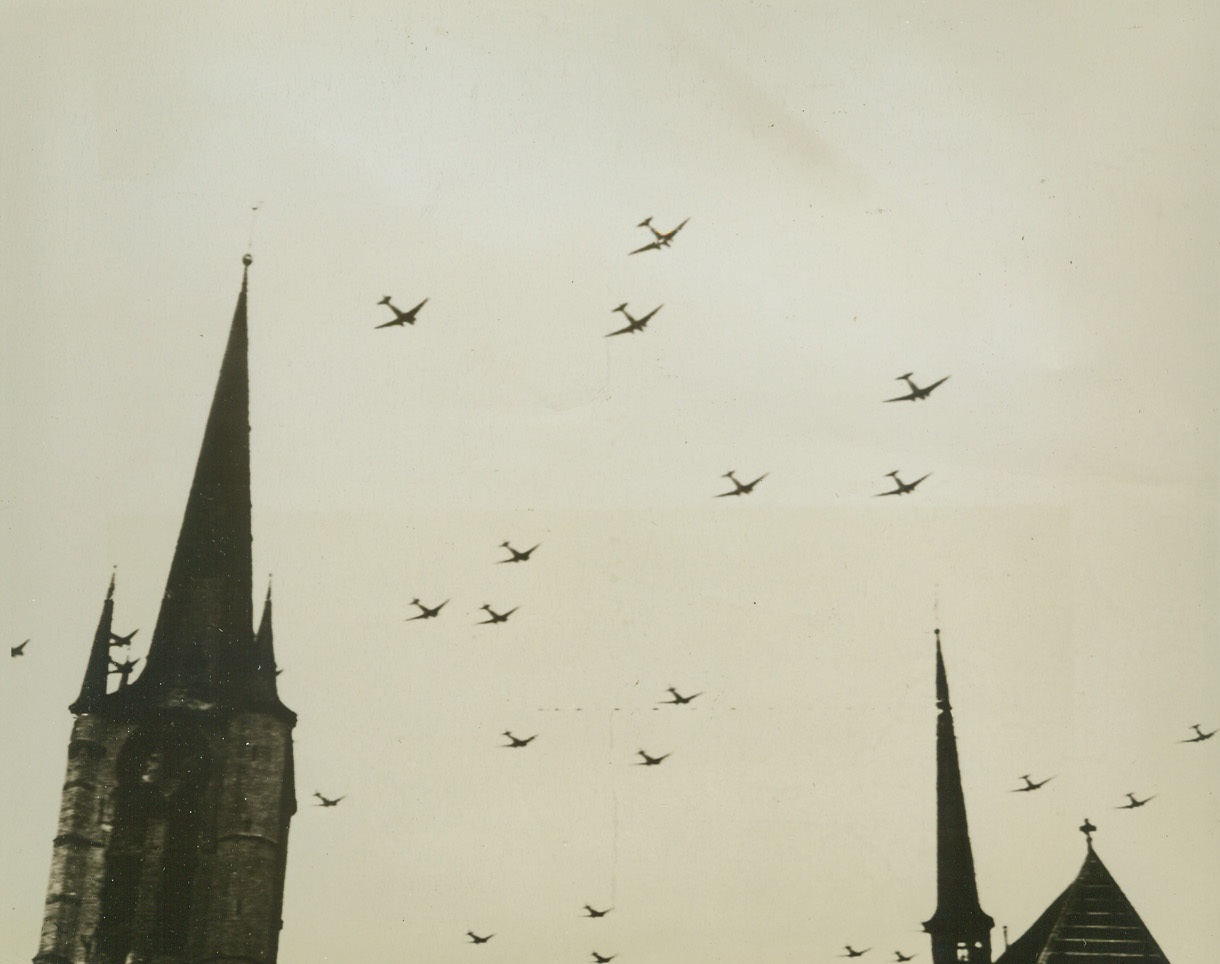 Sky Troops Over Belgium, 9/18/1944. GHEEL, BELGIUM – Like a fleet of black birds, Allied troop carriers roar over the spires of Gheel, en route to the “drop” area in Holland. Staging the surprise airborne invasion of September 17th, these warbirds were only a small part of the vast armada that sent thousands of Allied warriors into the lowlands. Credit (British Official Photo Via U.S. Signal Corps Radiotelephoto from Acme);