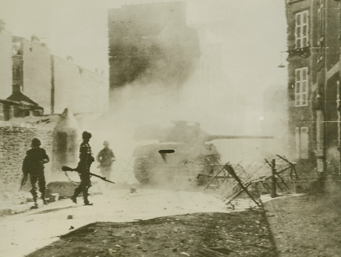 Point Blank Persuasion, 9/18/1944. Brest, France – With neither time nor patience for gentle persuasion, this Yank M-10 tank wins an argument with a Nazi pillbox emplacement in the streets of Brest, with its 76mm gun doing all the talking at point blank range. Behind the smoke-hung vehicle, infantrymen await the signal to advance. Credit (Signal Corps Radiotelephoto from Acme);