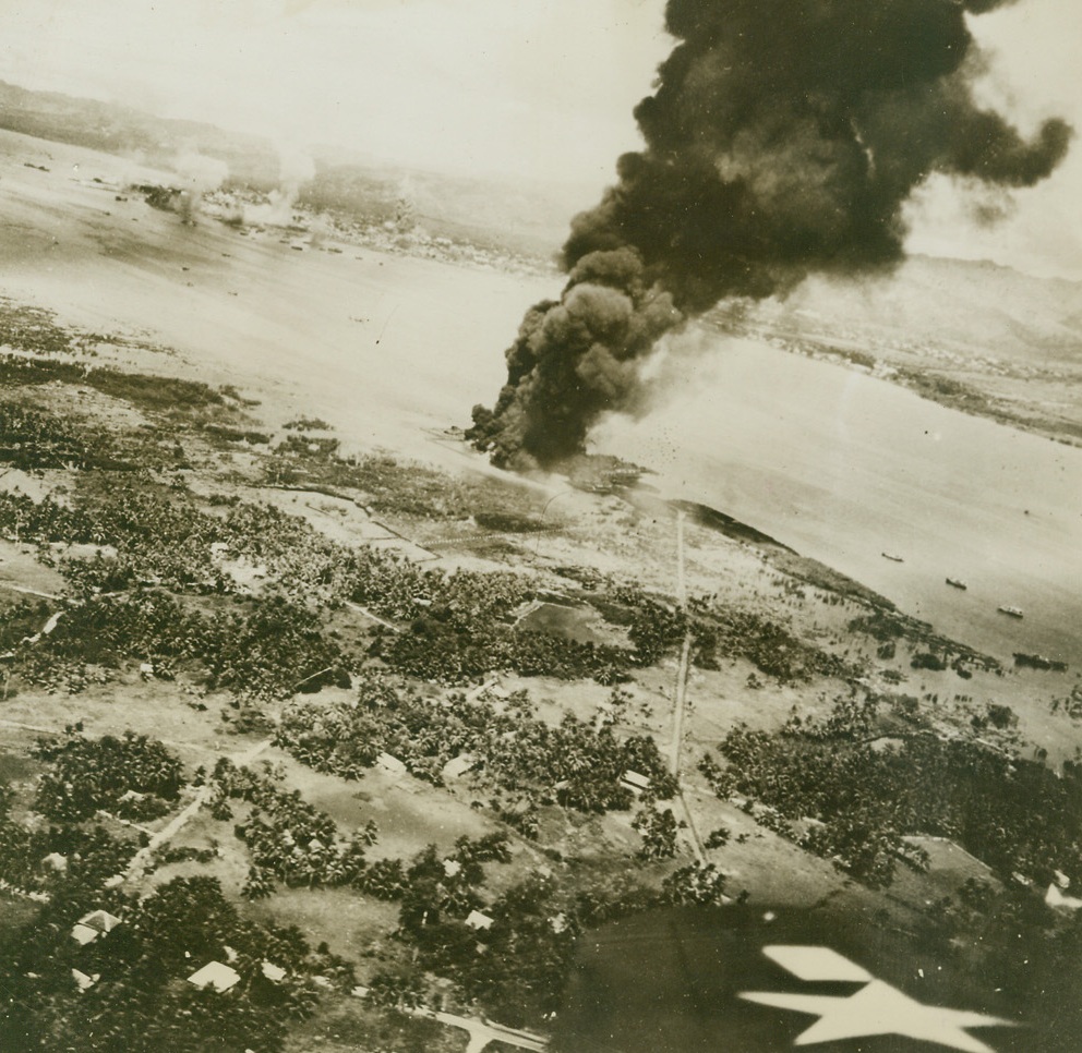 YANKS RETURN TO PHILIPPINES, 9/26/1944. CEBU, PHILIPPPINES—The wing of a Navy plane (right foreground) signifies the return of avenging Yanks to the Philippines, as an oil storage dump at Cebu burns fiercely after carrier planes from Adm. Halsey’s Third Fleet struck at the islands, in the first step of the American drive to recapture the island doors to Japan. Credit (Official US Navy Photo from ACME;