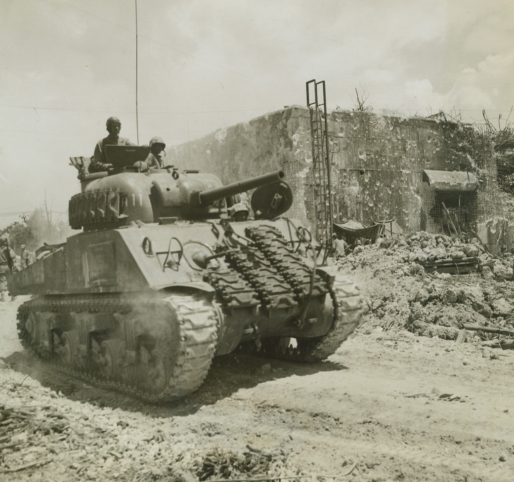 MARINES TAKE OVER JAP BLOCK HOUSE, 9/26/1944. PELELIU IS.—An American Sherman tank rumbles past this Jap blockhouse, filled with gaping shell holes – proof of the number of hits necessary to put defending Japs out of action. This blockhouse is now being used as a First Aid Station by 1st Division Marines on Peleliu. After 12 days of fierce fighting, Marines on the island see complete victory in sight. Credit (ACME Photo by Stanley Troutman, War Pool Correspondent);