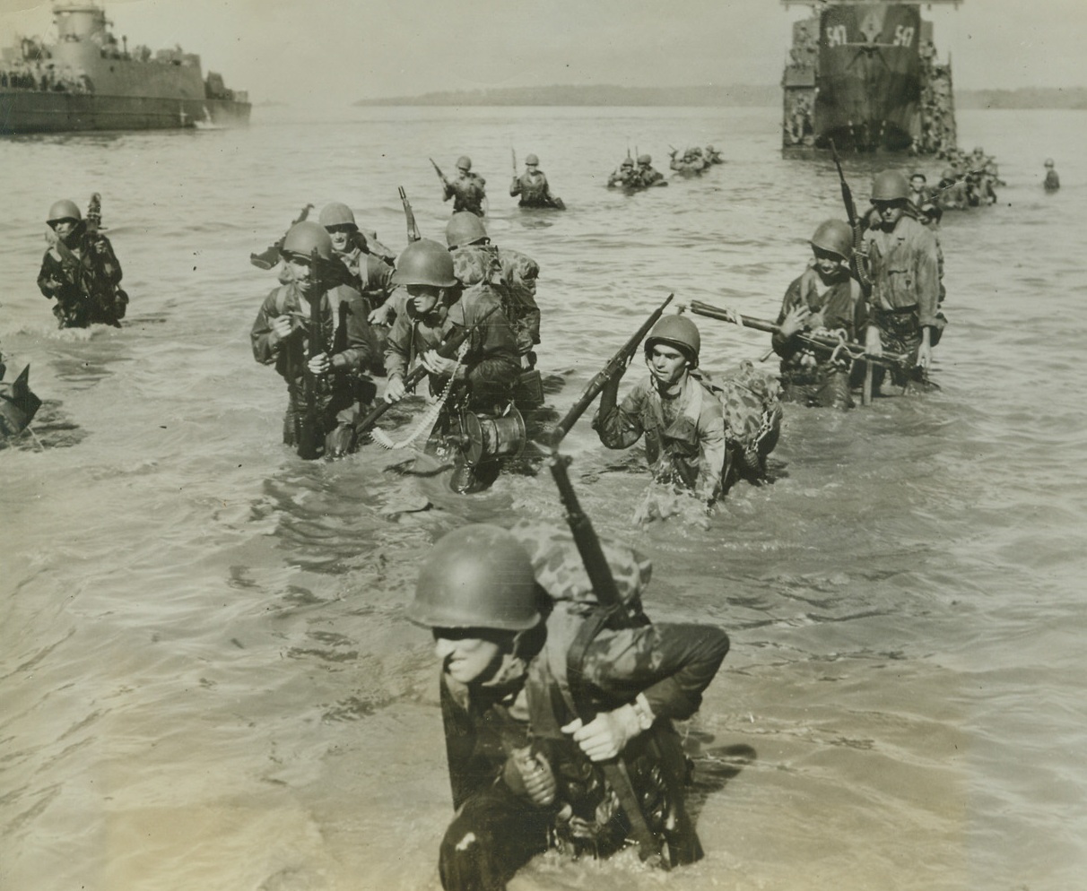 Yank Infantry Invades Morotai Island, 9/20/1944. Morotai Island – With “necklaces” of hand grenades and rifles, these Yank infantrymen swarm ashore in neck-deep water from their LCI’s to Morotai Island Beach, just South of the Philippines.  Credit line (ACME);