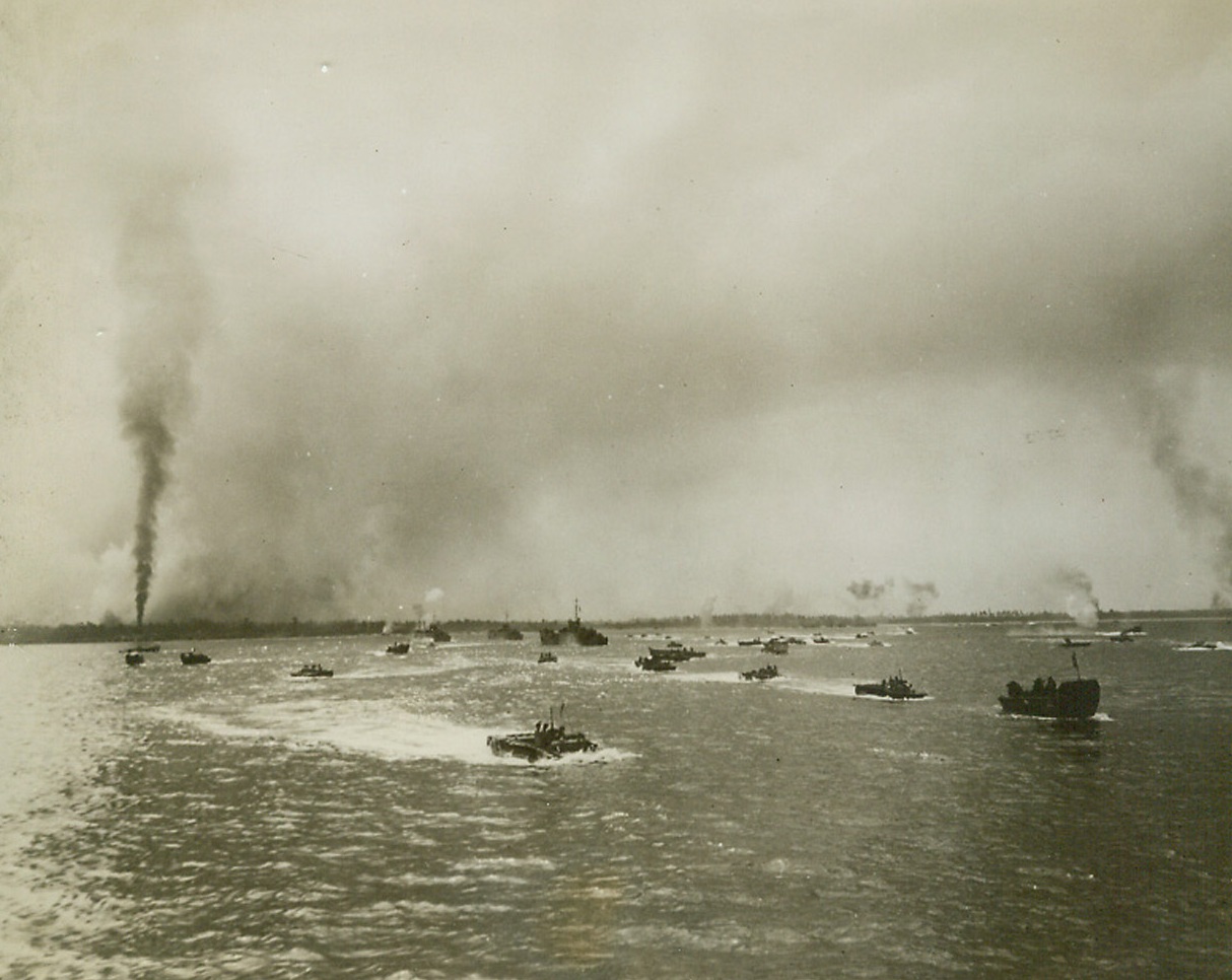 Two-Way Traffic, 9/30/1944. Peleliu Island, Palau – Churning the waters off Peleliu, many types of invasion craft pass each other as they chug toward and away from the besieged Palau island.  Enemy installations, targets of combined air and sea bombardment, go up in smoke along the beach as the full weight of the Sept 15th attack is felt. Credit line (U.S. Navy photo from ACME);