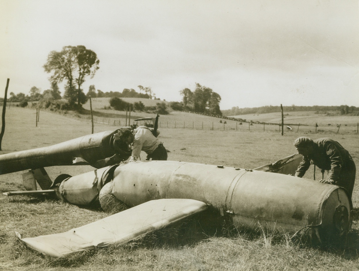 Robomb Misses Target by Long Sight, 9/8/1944. France—A flying bomb intended for England missed fire and traveled only a short distance from its launching site to land in a field in France. Somewhere in the Pas de Calais area, “Raymond” (left), of the French Resistance Movement, and Sgt. H.A. Barnet, Montreal, Canada, examine the V-I weapon which is almost intact.  Credit: ACME.;