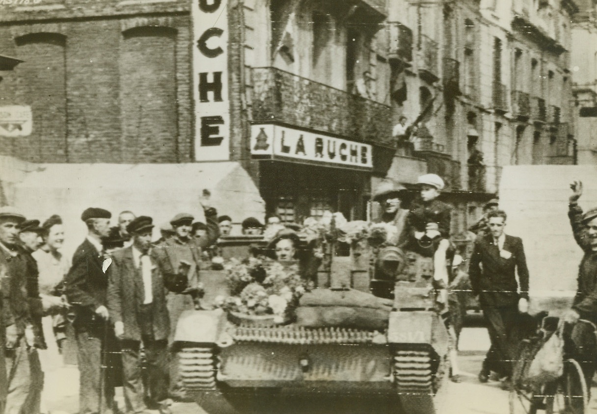 NO PAUSE FOR ONRUSHING CANADIANS, 9/5/1944. DIEPPE, FRANCE – A Canadian carrier, with flowers decorating its front, passes through a road block in Rue De La Barre, Dieppe.  Inhabitants cheer the soldiers, who, without so much as a halt, swept on to Le Treport and Abbeville.Credit: Acme;