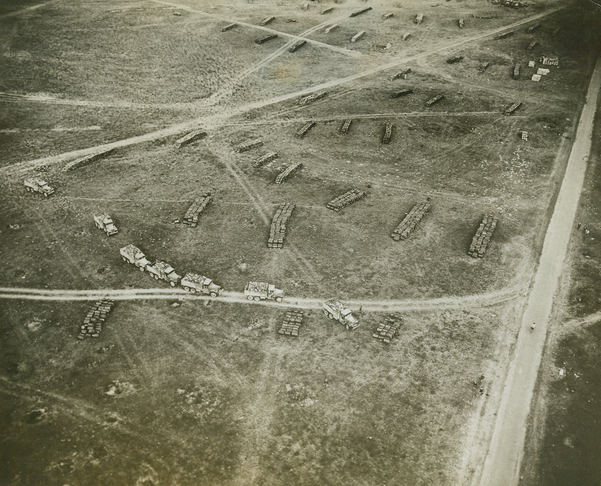 ALLIES ON THE MOVE, 9/23/1944. FRANCE – This air view of an ammunition dump in France gives a bird’s-eye view of the allied armies on the move.  A line of trucks are collecting supplies to be transported to the front lines to keep pace with the rapidly-moving armor.  Scattered over the ground are stacks of ammunition and supply crates waiting to be picked up. Credit: Acme;