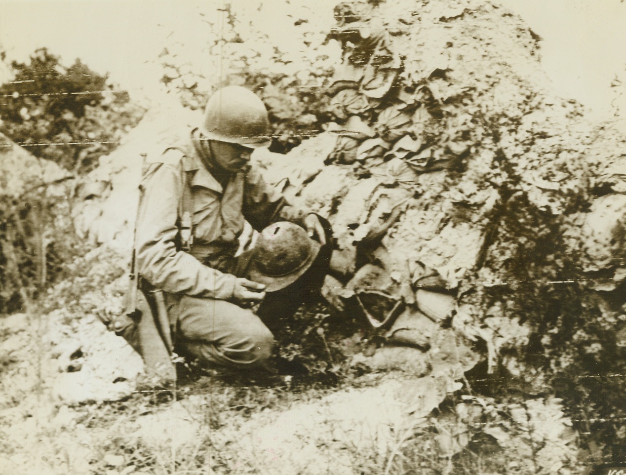 Mute Reminders of Another War, 9/7/1944. Argonne, France – As Americans fought on battlefields which still bore marks of another war, Sgt. Fred Owens, Los Angeles, Calif., examines a battered old French helmet from World War I which he found beside a pile of rotting sandbags in the Argonne Forest. Credit: Signal Corps Radiotelephoto from ACME;