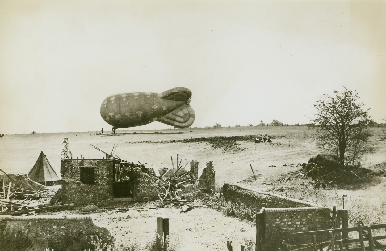 First Down, 9/11/1944. England – The first flying bomb brought down by a barrage balloon landed in this area, tearing a huge crater in the ground. The demolished barn in foreground is the only bit of destruction accomplished by the vengeance weapon, which was heading for a crowded urban area before it was intercepted by the balloon. Credit: British Official Photo from ACME;