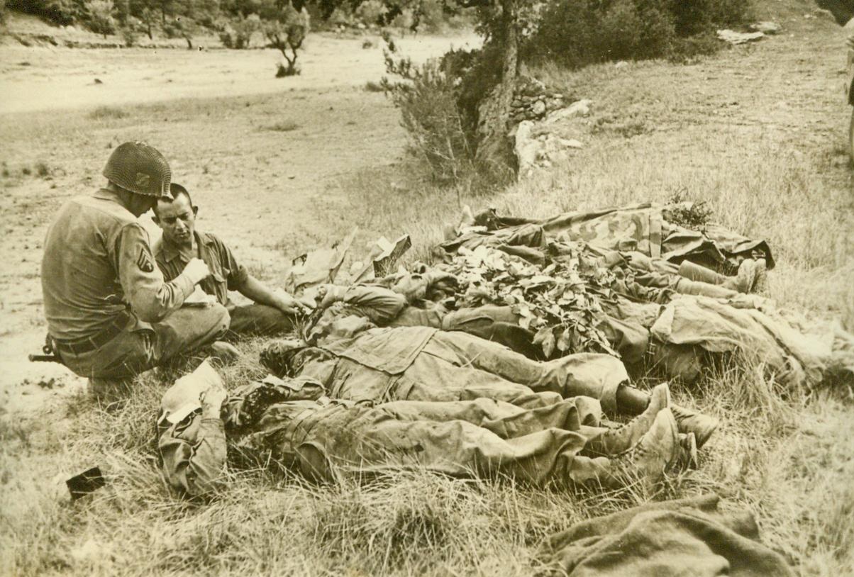 Death Knows No Discrimination, 9/9/1944. Southern France—Two American soldiers go about the grim job of identifying their dead, who lie on the slop of a mountainside in the south of France together with Germans who were killed in the battle for Aix-En-Provence 9/9/44 (ACME);