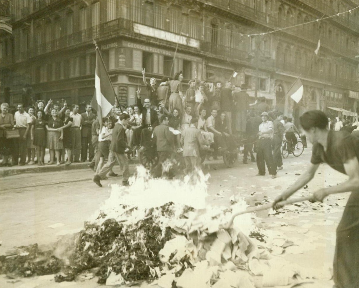 Victory Parade In Marseille, 9/9/1944. France -- While one Frenchman at right sets fire to torn German propaganda pamphlets, other residents of Marseille stage an impromptu victory parade down famous Canebiere riding a wagon, waving the Tricolor and wildly cheering the liberation of the great Southern French port from the Hun. The V-for-victory symbol is once again displayed by the jubilant Frenchmen -- This time as free men.  9/9/44 (ACME);