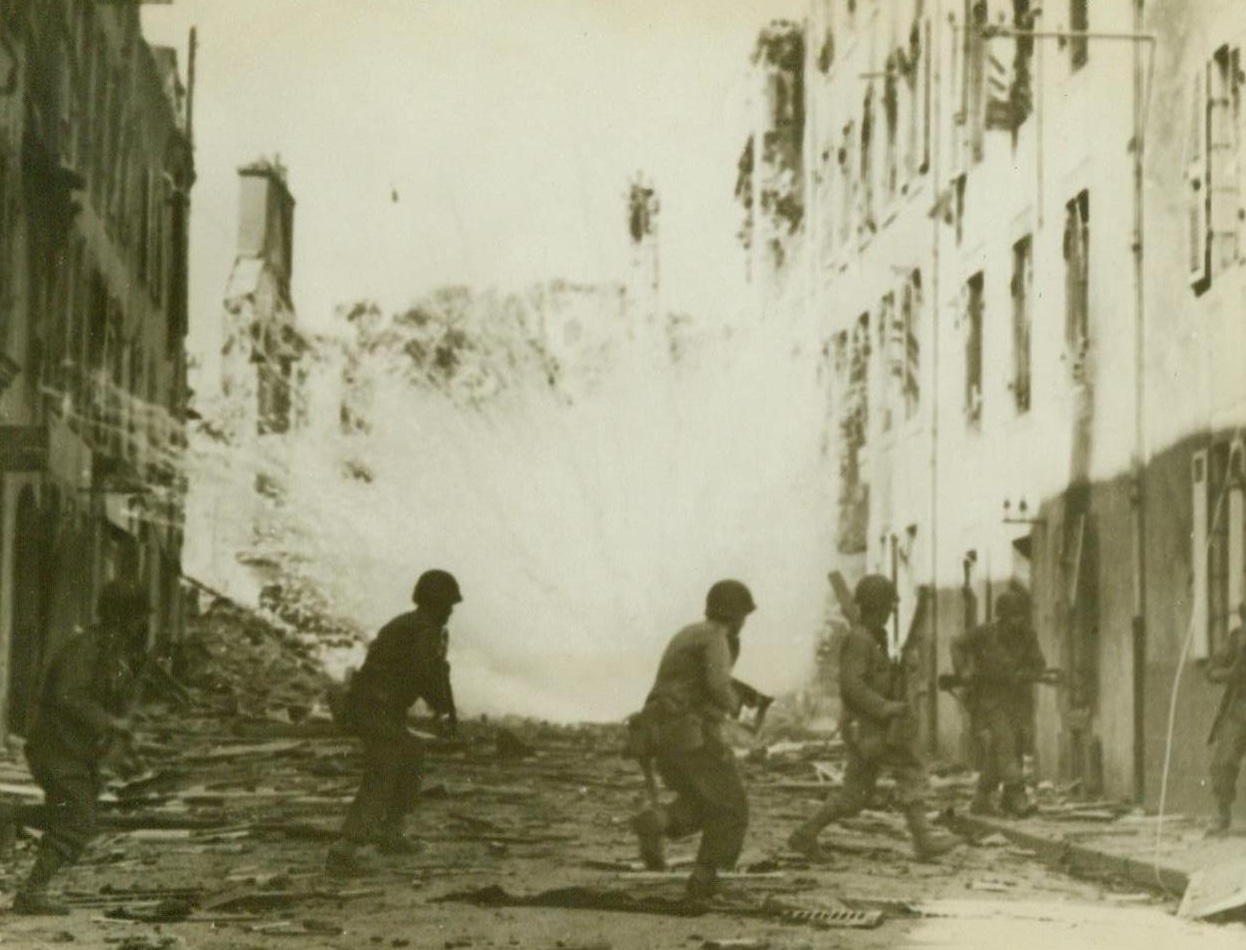 Yanks Fight In Face Of Fire, 9/23/1944. France -- American soldiers in the French port of Brest, now captured, dash across a street as a white phosphorus shell explodes almost in their midst. Bitter street fighting marked the final taking of this strategic city by American forces. 9/23/44 (ACME);