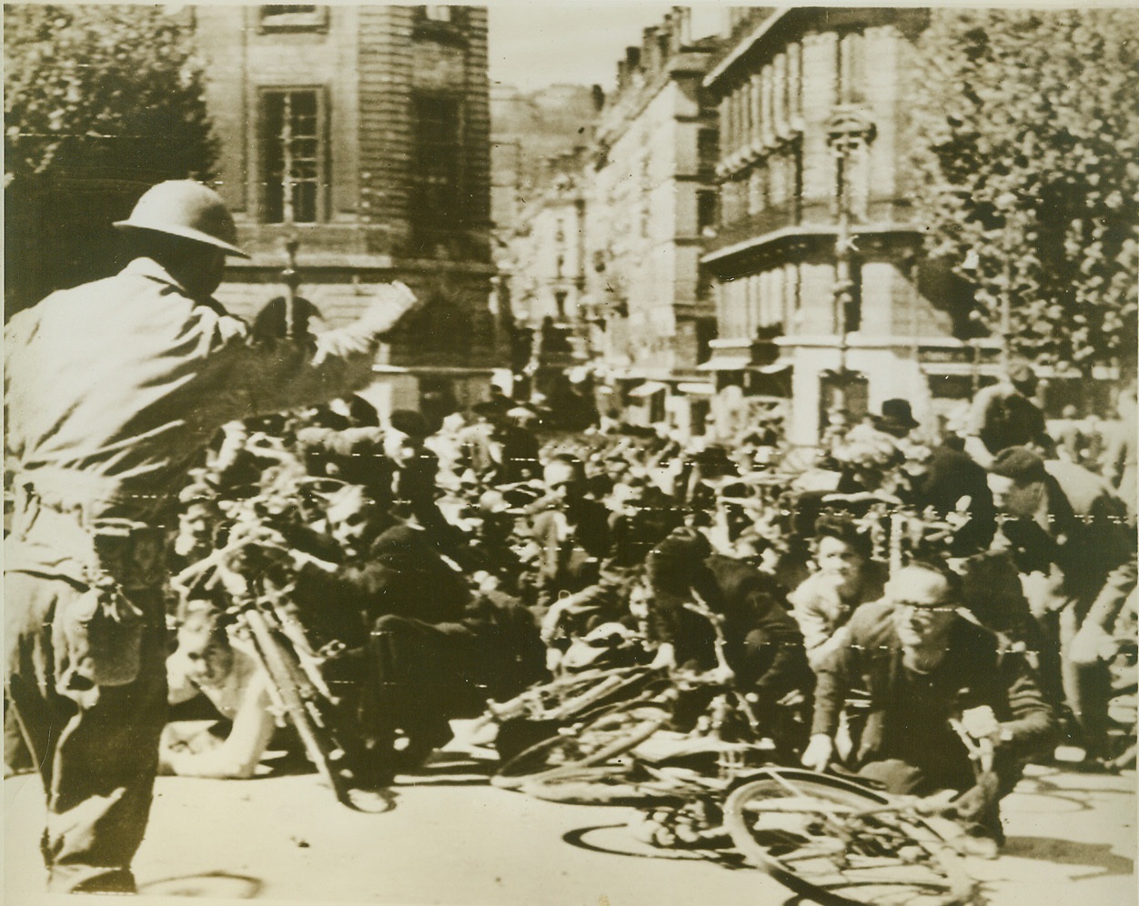 Crowds in Lyon Dodge Nazi Bullets, 9/6/1944. France—An Allied soldier urges panic-stricken crowd to hug the ground as 7th Army soldiers and members of the marquis battle armed Nazi sympathizers barricaded in the tower of the Lyon General Hospital after the city fell. This scene is on the bridge crossing the Rhome River. Credit: ACME photo via army radiotelephoto;