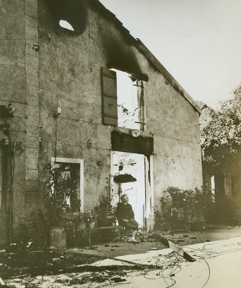 Burned Out But Unbeaten, 9/30/1944. Angirey, France – Quietly resting in the shade, an old woman of Angirey sits outside the remains of her ruined café. Retreating Germans burned out the entire town before the Allied Seventh Army entered. 9/30/44 (Signal Corps Photo From ACME);