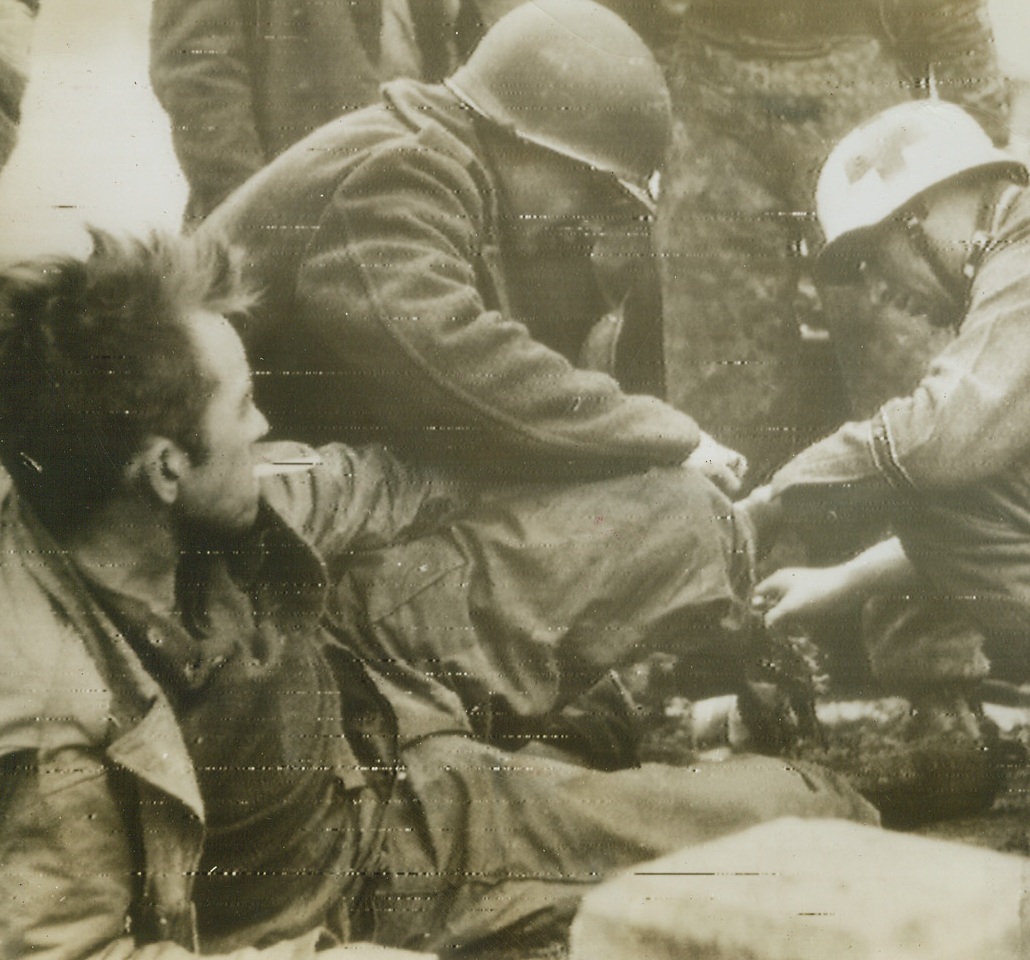 Wounded Yank Prisoner #2, 1/3/1945. Western Front—The same wounded American prisoner (see photo #R747111) is having his foot dressed by a fellow prisoner and a German Red Cross worker. In the foreground, according to German caption, is a concrete tank obstacle on the Siegfried Line. This photo was received by radio from Stockholm today. Credit: ACME radiophoto.;