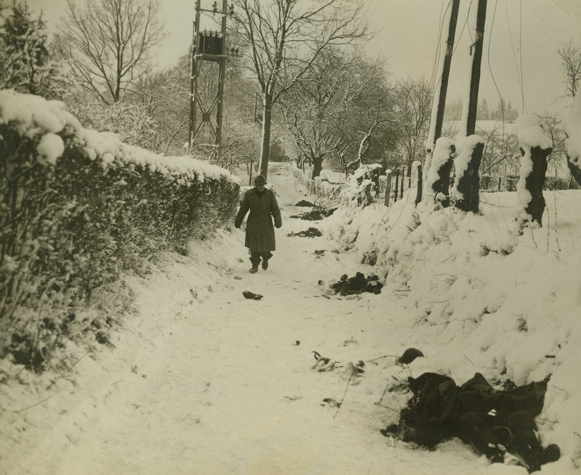 THEIR DEATH WARRANT, 1/14/1945. BELGIUM—When the Germans staged the recent counterattack in Belgium, the move practically sealed their death warrant. Here, a Yank walks down a street of a Belgian town and surveys the bodies of dead Germans lying in the snow, killed as they tried to keep the town from being recaptured by troops of the 82nd Airborne Division of the US Army. Photo is by Harold Siegman, Acme War Pool Correspondent. Credit: Acme;