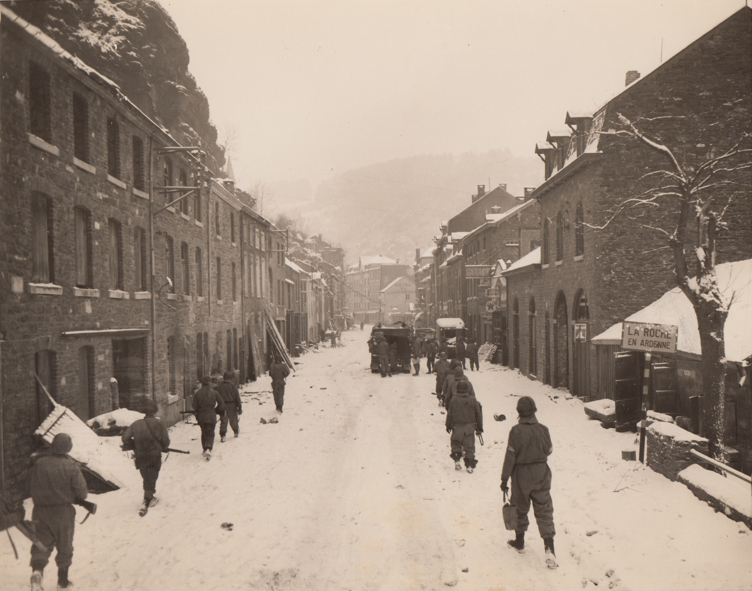 YANKS ENTER LA ROCHE, 1/19/1945. BELGIUM—Snow still falls on the battle-scarred town of La Roche as American soldiers enter after Nazis had been driven into the hills. Yanks walk in single file on both sides of road.;