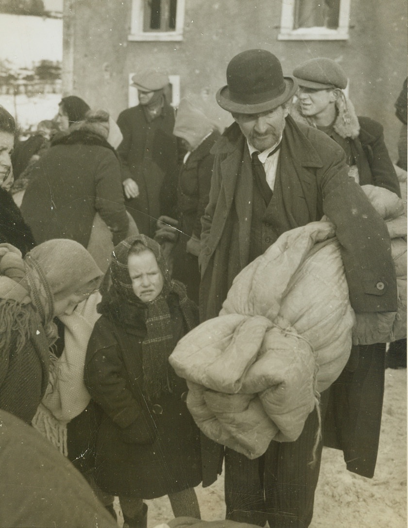 Evicted by War, HARLANGE,  1/21/1945. BELGIUM -- Bent under the weight of his blanket roll, this citizen of Harlange holds the hand of his little girl, who is weeping bitterly, as they wait, with other Belgians, for trucks which will take them from Harlange to safety behind the battle lines. Photo by Charles Haacker, Acme war pool correspondent. Credit (ACME) (WP);