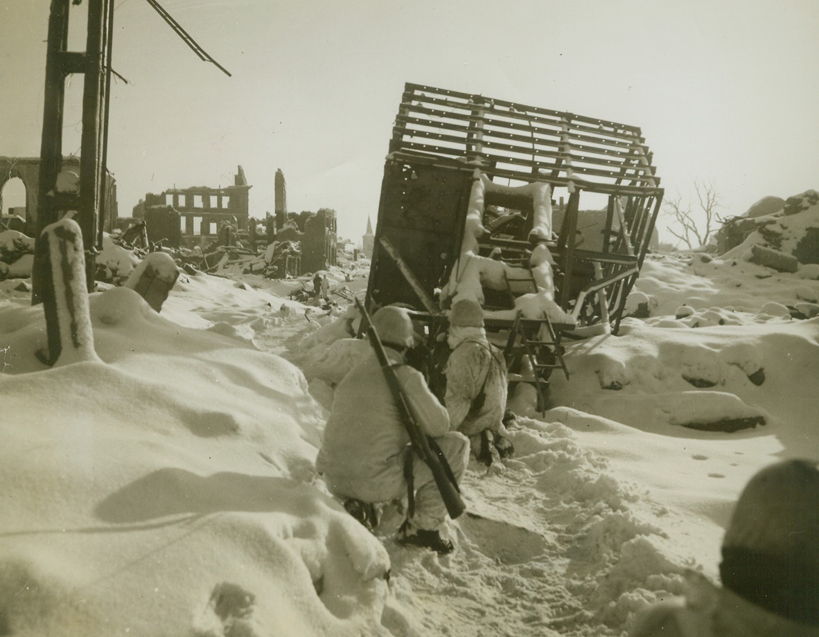 St. Vith Street Scene, 1/31/1945. ST. VITH, BELGIUM – The wreckage of buildings, blanketed by a smooth cover of new snow, obliterates this street in embattled St. Vith. White-clad infantrymen, dug in amid the debris, keep an eye peeled for snipers in the newly captured town. Photo by Harold Siegman, Acme photographer for the War Picture Pool. Credit Line – WP- (Acme);