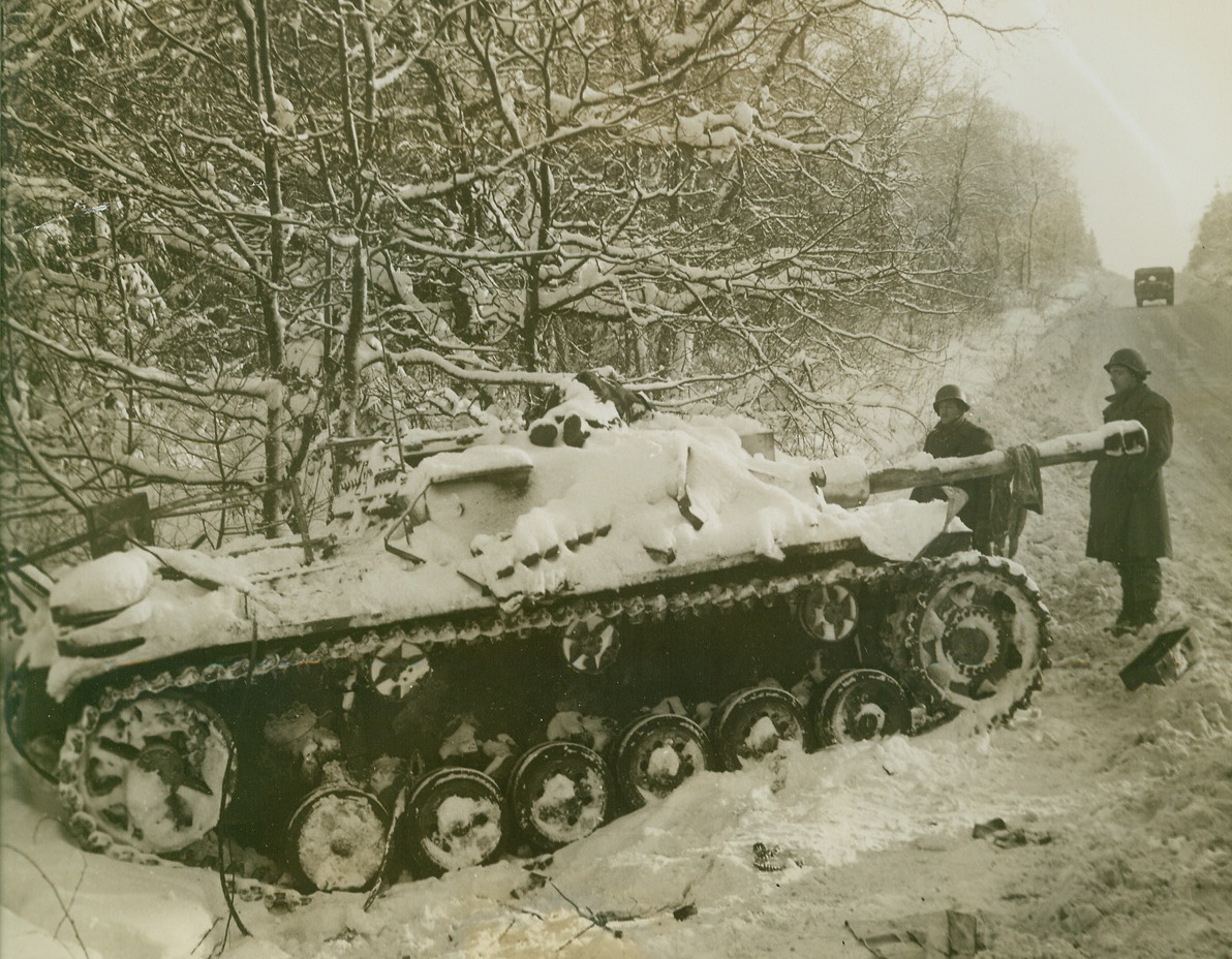 Death’s Corner, 1/31/1945. ST. VITH, BELGIUM – Death struck often and mercilessly in this embattled corner of the world, as Yank First Army infantrymen fought for possession of snowbound St. Vith. Two Americans examine a knocked-out Nazi tank, atop which a dead German lies. Photo by Harold Siegman, Acme photographer for the War Picture Pool. Credit Line –WP—(Acme);