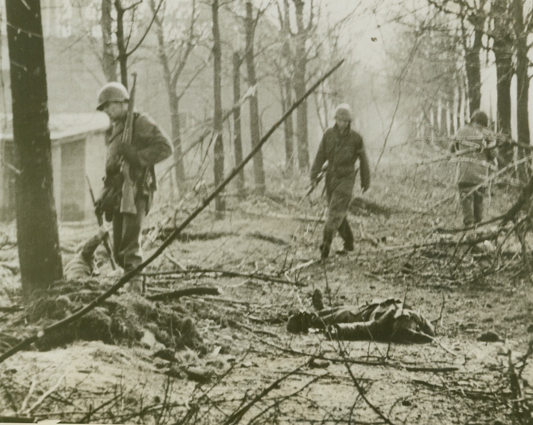 They Cornered Him – So He Bit, 3/3/1945. ROER RIVER, GERMANY – These three American soldiers stagger around dazed from the repercussions of a hand grenade which a German prisoner, captured during the Roer River crossing, lies dead in the foreground. A badly wounded GI behind the three at left is leaning on his rifle in an effort to get to his feet. The fellow standing makes no effort ot help him because he, too, is badly wounded (not peculiar way he holds his rifle.)Credit (ACME) (WP);