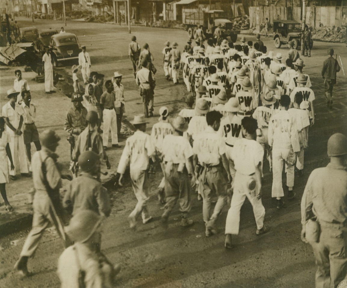 Destroyers Help Rebuild, 4/10/1945. Manila—Japanese prisoners of war, identified by the letters “PW” on their backs, march down Rizal avenue on the way to their daily work of clearing up the wreckage of sections of Manila they, and their Nip comrades wantonly destroyed as the Yanks were taking the …. U.S. military police guard the group. Credit line (ACME);