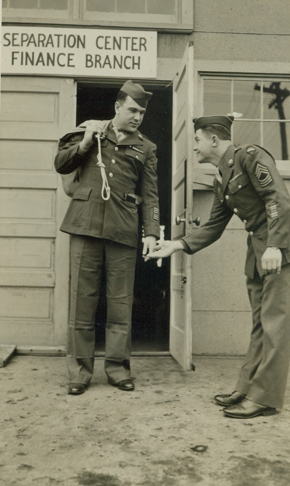 Farewell to Arms, 5/12/1945. Fort Sheridan, Ill. – Sgt. Rudolph Kolenic (right), of Muskegon, Michigan, one of 200 veterans demobilized today (May 12) at Fort Sheridan under the new point-discharge system, executes a courtly bow as Corp. Richard Lockhart, Ironwood, Michigan, credited with a score of 126 points—highest at Fort Sheridan—leaves for home, once again a civilian. Credit: ACME;