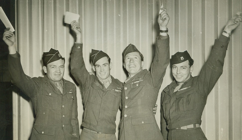 CIVVIES, HERE WE COME!, 5/12/1945. JEFFERSON BARRACKS, MO.—Flourishing their score cards, visual testimony of their 85 points or better, score that entitles them to honorable discharge from the service under the new point-discharge system, these vets are among the first to be processed at Jefferson Barracks. Left to Right: T/Sgt. Henry Bast, Cedar Falls, Ia.; T/5 William Archer, Mystic, Ia.; T/Sgt. Arthur Isenberg, Pleasantville, Ia.; S/Sgt. John Fitzgerald, Ames, Ia. Credit Line (ACME);