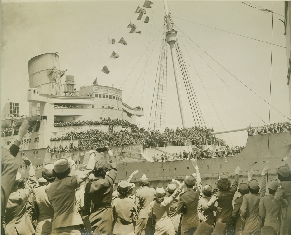 WELCOME HOME, BOYS!, 7/11/1945. NEW YORK – Returning soldiers jamming the decks of the giant transport Queen Mary get enthusiastic welcomes from Red Cross workers filling the pier. The Mary, one of eight transports which docked in New York today, carried 15,642 troops, including 7,000 members of the Canadian First Army, who boarded special trains for Canada immediately after docking. Credit: ACME;