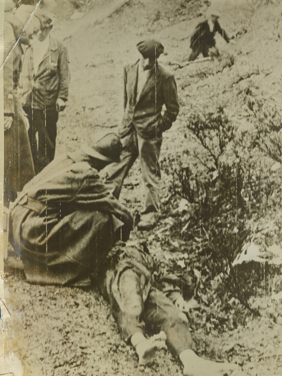 End of the Road. Washington, D.C. – This Nazi reached the end of his road on this hill in Corsica, where he fell before French patriots. here a French Intelligence officer, with the rank of Lieutenant, remove the dead German’s identification tags, as Corsican civilians look on. Picture flashed to the United States by Signal Corps RadioTelephoto;