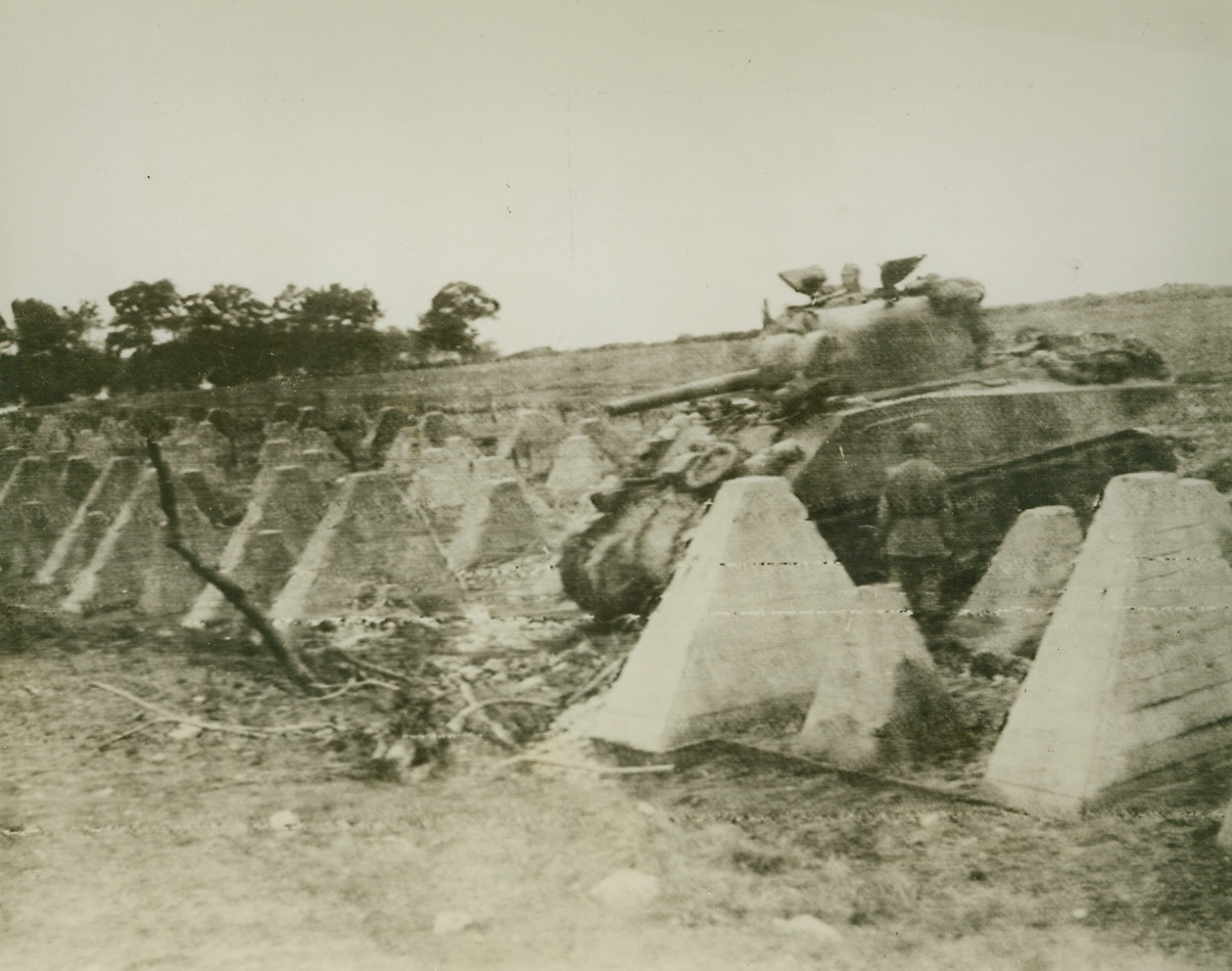 Siegfried Line Pierced. Germany—Following a path blasted by U.S. Army engineers, an American tank passes through a belt of steel and concrete dragons’ teeth, obstacles in the vaulted Siegfried line near Aachen, Germany. Yank troops went on to finish the job by smashing through the second belt of fortifications. Photo by Andrew Lopez, ACME photographer for the War Picture Pool. Credit: ACME photo via Army radiotelephoto.;
