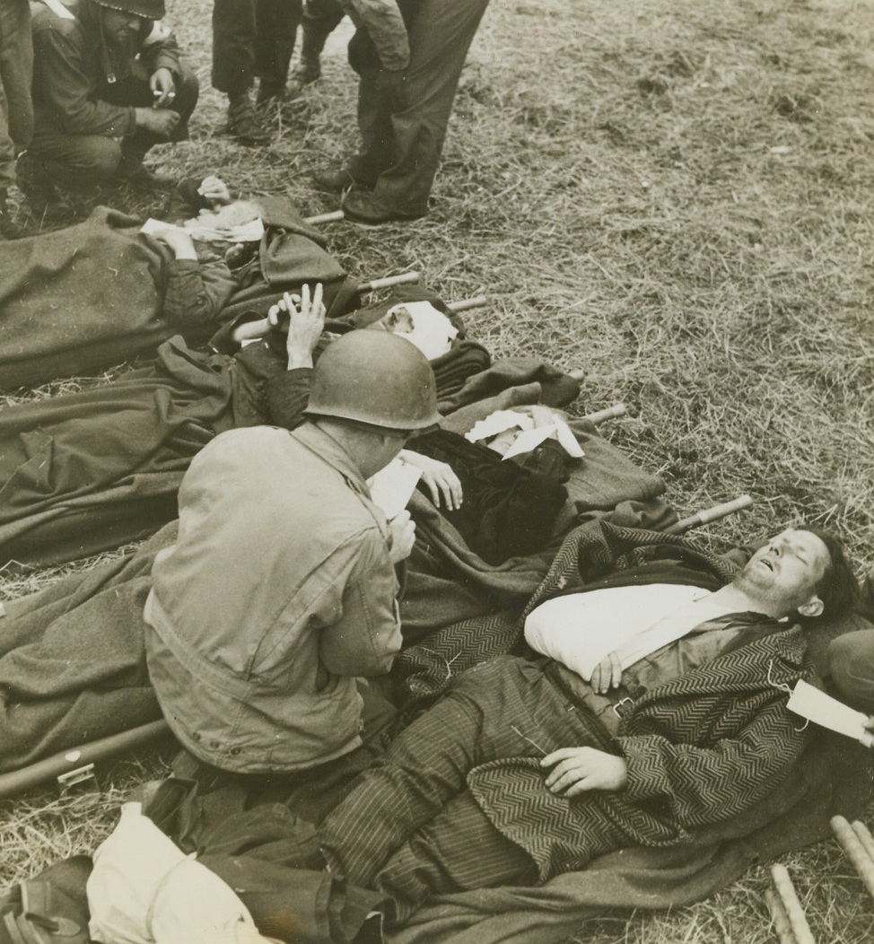 INNOCENT VICTIMS OF THE WAR. FRANCE—French civilians, both men and women, who were wounded during invasion fighting, are given treatment by US Medical Corpsmen. These people will eventually be shipped to hospitals with the other casualties.Credit: Official Navy Photo from Acme;