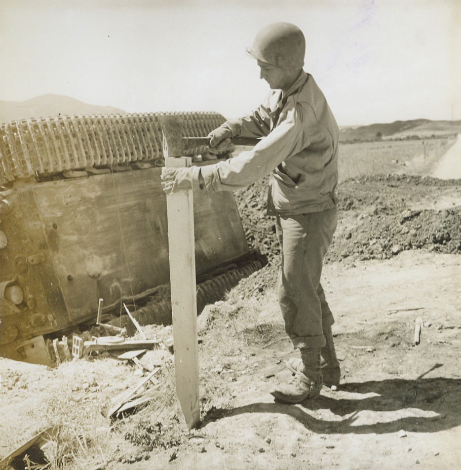 SAFETY POSTS FOR ITALIAN ROADS. Pvt. Omero Del Papa of Galveston, Texas, drives a safety post into the edge of an Italian road, next to an overturned German tank.;