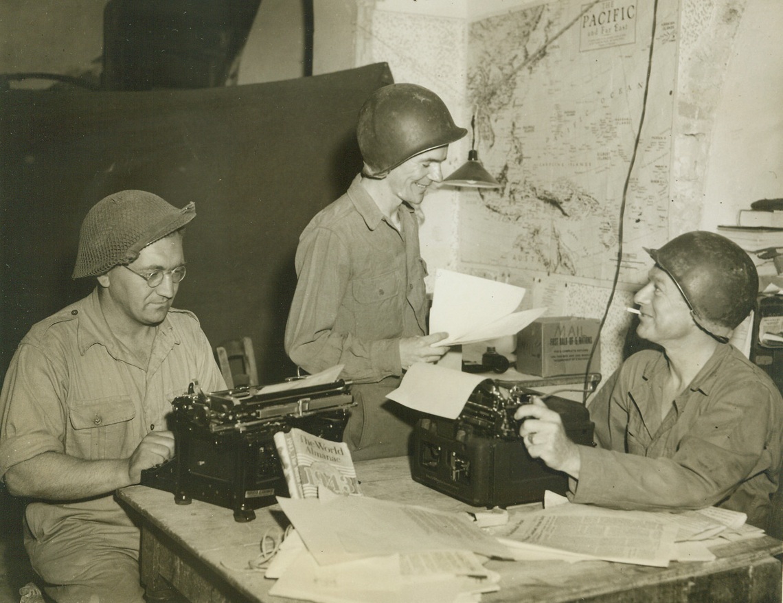 Dispatches from the Front. ITALY – And here the front is uncomfortably close for this photo shows the news section of the newly inaugurated Anzio paper, called the Beach Head News, which is written for and by front line troops. It has four pages printed on a linotype machine, portable and miniature, of course. Looking over dispatches are Gunner Hargrave Andrew, London, England; Corp. Roger Flaherty, Norwood, Mass.; and Sgt. Frederick Bell, Pecos, Texas.;