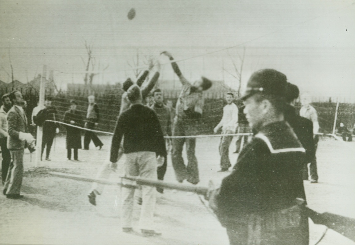 No Title. Reproduced from Japanese English-language propaganda magazine “Freedom,” published by Japs at Shanghai to give their version of internment of U.S. subjects pending their exchange, photo above is described by Japs as “play time” scene at a war prisoners’ camp “somewhere in Shanghai,” and shows prisoners playing volley ball under armed guard.;