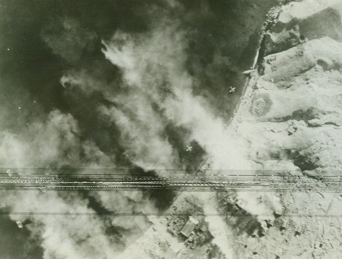 No Title. Fierce fires rage from Jap seaplane hangars set fire by U.S. Army Air Force bombing raid on the Japs’ Kiska, Alaska Camp area. Thru smoke from burning installations may be seen planes and boats in water.  Credit: U.S. Army Air Force photo from ACME.;