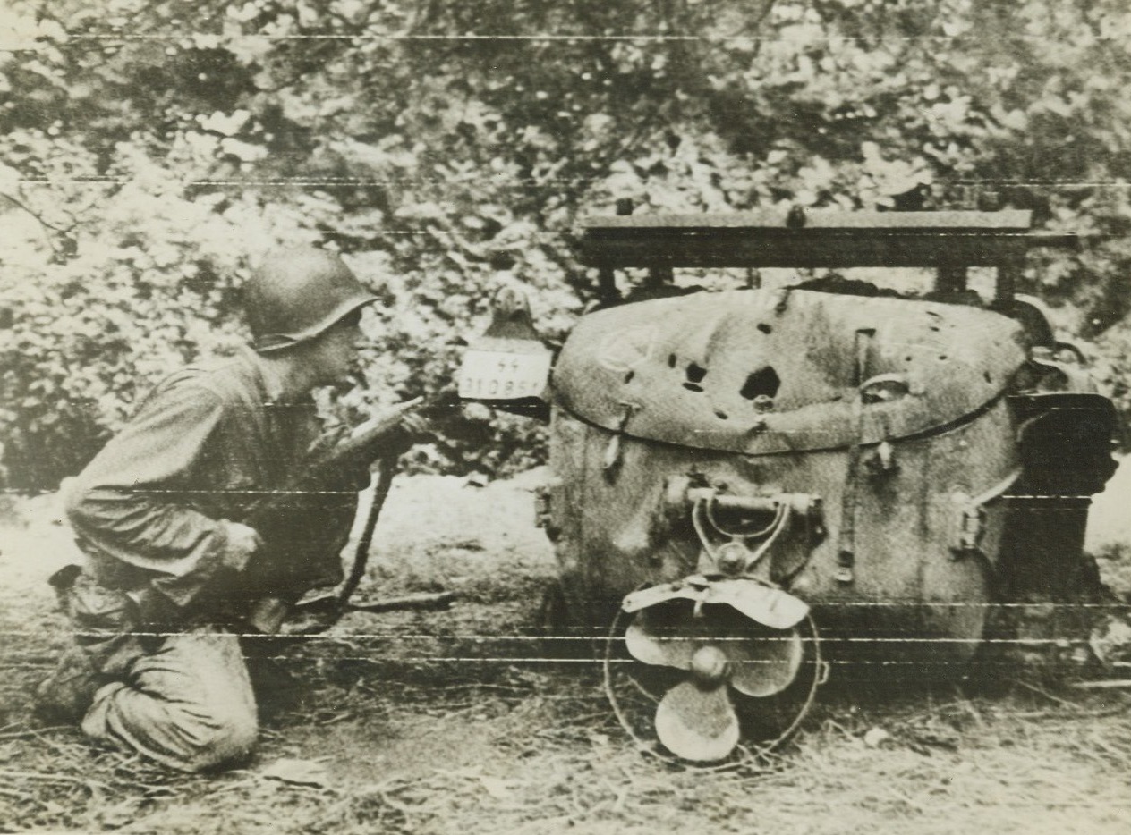 NAZI JEEP PROVIDES COVER FOR YANK, FRANCE –An American infantryman kneels low behind an overturned German amphibious jeep, taking cover from enemy fire at the front in France.  The doughboy keeps this rifle on the ready, set to return fire that comes his way.Credit: Acme;