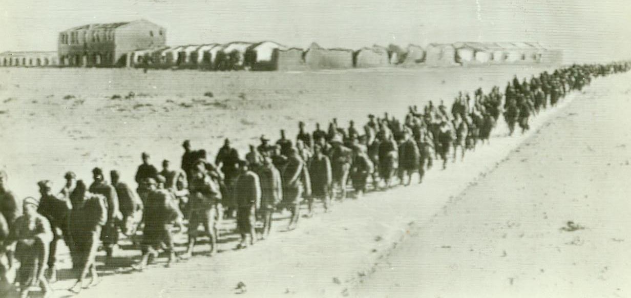 No Title. Ruins of their base (Sidi Barrani) in background, some of more than 10,000 captive Italians march away to British prison camp.;