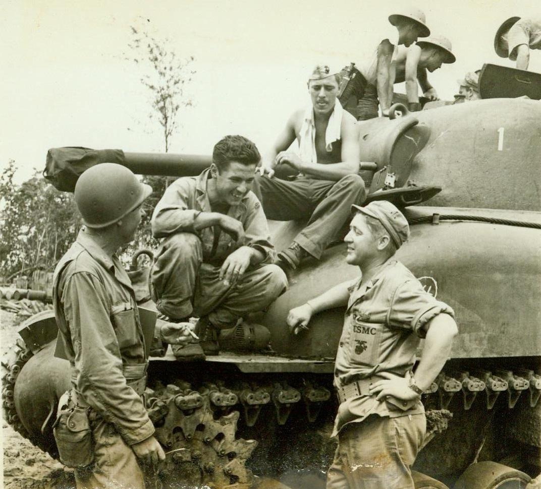 Before the big push. SOMEWHERE IN NEW GUINEA – Waiting to leave a staging area somewhere in New Guinea for the invasion of New Britain, a group of doughboys and war correspondents chew the fat beside an Army tank. In the foreground are: Artist Gary Sheahan (left) of the Chicago Tribune, and Frank Prist. Jr., ACME Newspicture Correspondent (right). CREDIT LINE (ACME);