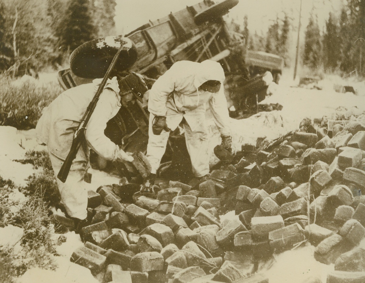 Russian Food Truck Captured by Finns, 1/10/1940  FINLAND – Finnish “ghost” soldiers inspecting a large quantity of Russian black bread, captured by the Finns when they attacked a Soviet supply column. A wrecked food truck is shown in the background. Credit: (ACME);