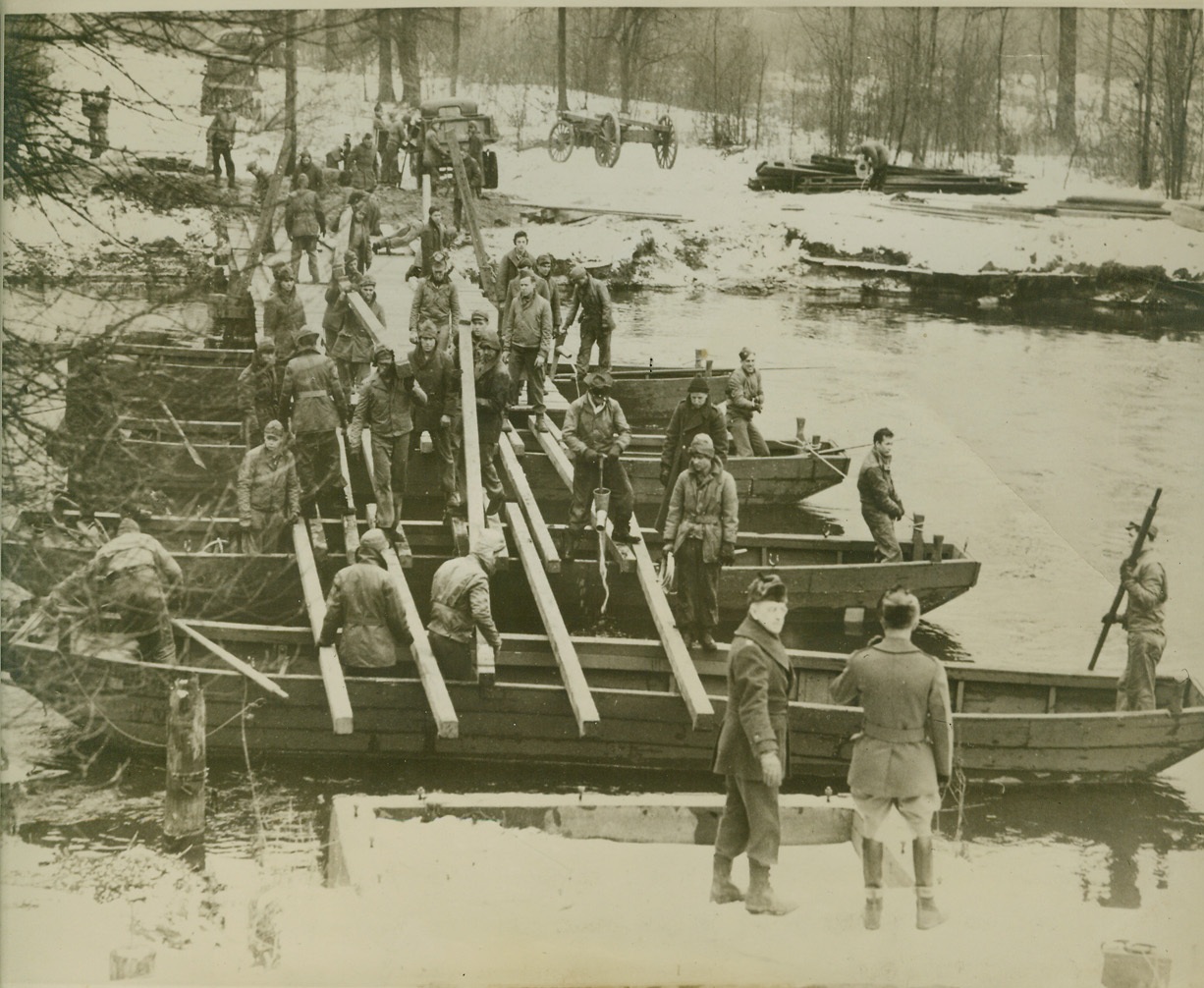 BRIDGES MADE WHILE YOU WAIT, 1/17/1940  FORT CUSTER, MICH. – When HQ of 5th Division found they needed a bridge across the Kalamazoo River to have access to Fort water they didn’t wait for the new steel bridge to be finished. Using available material and 15-year-old pontoons, the engineers had this bridge ready in three hours. Credit: OWI Radiophoto from ACME;