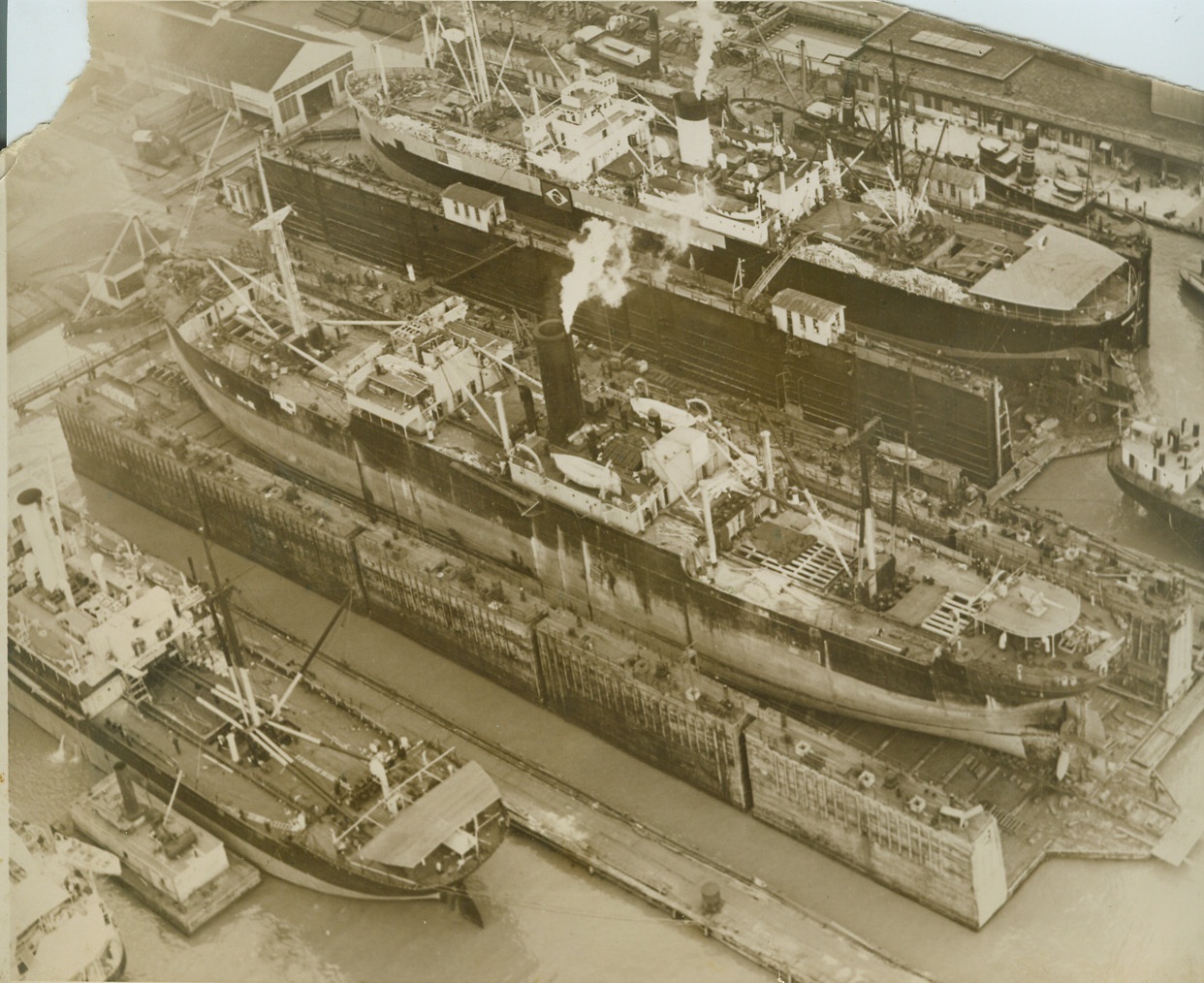 BRITISH SHIPS FITTED WITH ARMOR PLATE IN HOBOKEN, 4/25/1940  HOBOKEN, N.J. – A fine point involving the United States’ neutrality law has been raised with the disclosure that two British merchant ships are being fitted with armor plate in the Hoboken shipyard of the Bethlehem Steel Corp. The ships, one of which may be seen in center of this air photo with gun mounted on after deck, are having steel plates put on pilot houses, bridges and vital parts of the superstructures as protection against air bombs. It will be left to Secretary of State Cordell Hull to decide if this violates U.S. law. Credit: ACME;