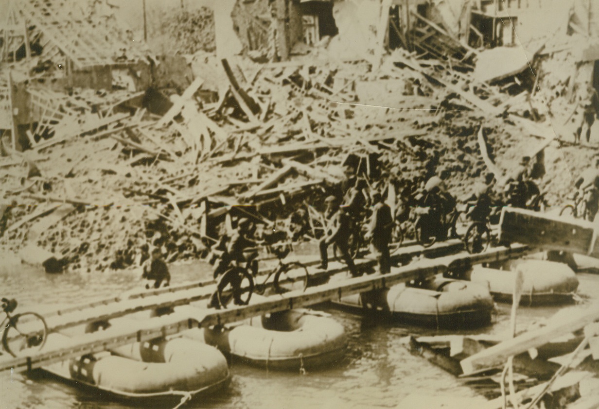 Advancing Through Belgium, 5/29/1940  BELGIUM—German bicycle units advancing over a pontoon bridge thrown across a river in Belgium at the spot where the retreating defenders blew up a bridge, according to German caption. Credit: ACME.;