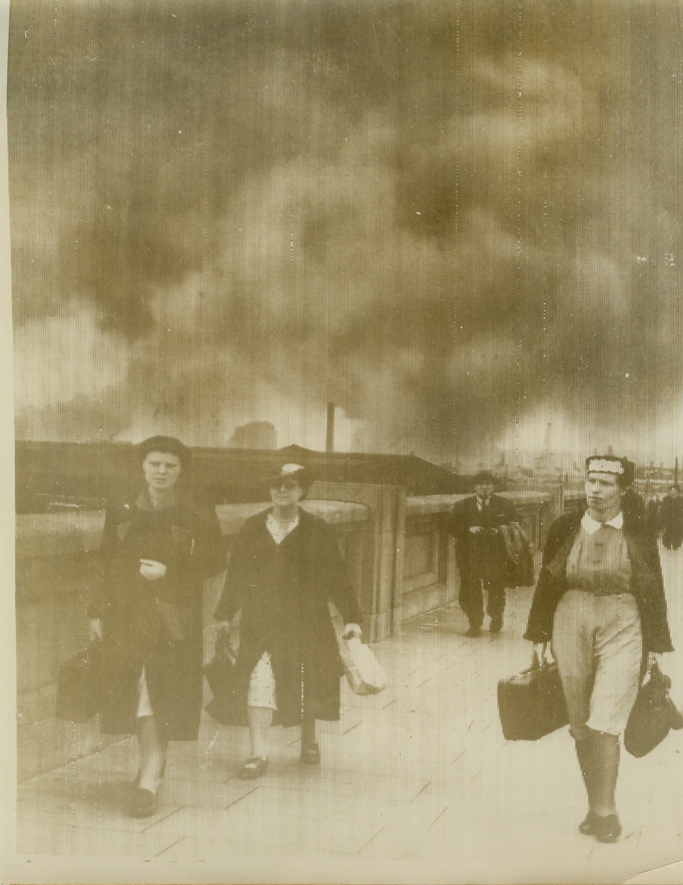 Women Leave Blazing Dock Area, 9/9/1940  LONDON -- Apparently not the least bit panicked by the German onslaught, these women, with faces set, leave the London dock area after air raids made it a blazing inferno. Some 2,000 residents of this area were evacuated from their flame encircled homes by a flotilla of pleasure craft that enacted a miniature Dunkirque. Photo sent from London by radio on Sept. 9th. Credit: (ACME);
