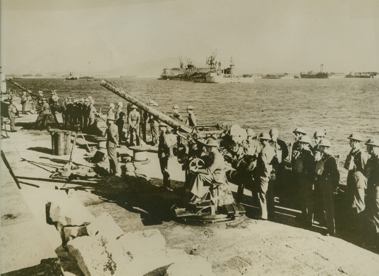 ON GUARD ON THE ROCK, 10/11/1940  GIBRALTAR—Gun crew lined up by their weapons on Gibraltar, Britain’s strategic fortress controlling the western entrance to the Mediterranean. Gibraltar has been bombed repeatedly by Italian planes and at lease once by French planes. It is often mentioned as an Axis objective, to be conquered by a drive from Spain. Credit: Acme;