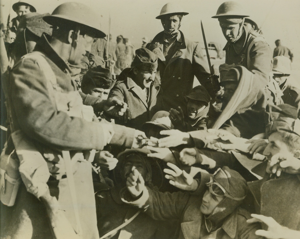 After the Battle: Italian Prisoners Get Smokes, 1/11/41  After the smoke of battle comes the smoke of cigarettes and Italian prisoners, captured by British in the Western Desert near Sioi Barrani, are shown reaching for cigarettes offered by one of their captors.;