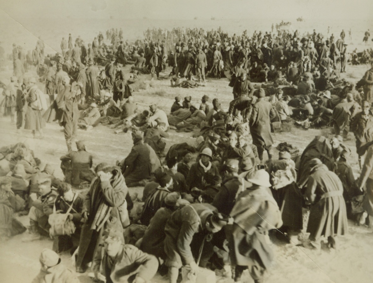Booked “for the Duration”, 1/13/41  North Africa—Some of the thousands of Italians taken prisoner by the English and Australian forces pushing into Libya await transportation to prison camps at an unnamed spot in the Western Desert. Photo made by the Australian army photographer, flown from Sydney to the U.S.  Credit: ACME.;