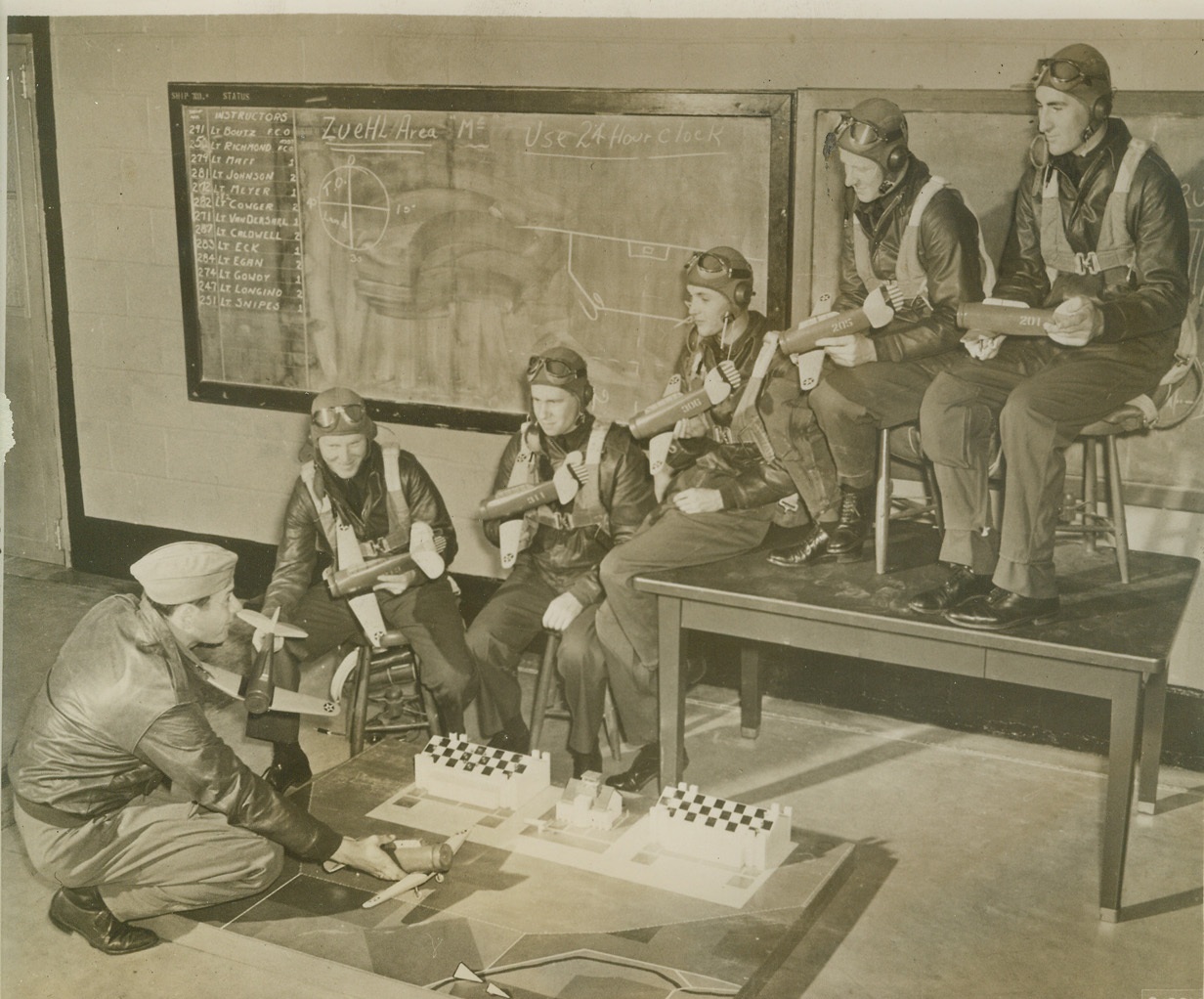 Training with Models, 1/28/41 RANDOLPH FIELD, TEXAS – Landing miniature air planes at the “West Point of the Air” on a tiny airport seems rather silly, but actually it serves a definite purpose in illustrating the proper aerial traffic pattern to be followed. With as many as 300 planes aloft at once, rigid air discipline must be maintained. Lieut. Lloyd W. Sheppard, of Mill Valley, Calif., explains correct technique for a 180 degree approach to student pilots (left to right) George C. Salvo, Charleston, S. Car.; Samuel A. Swanzig, Versailles, Mo.; H.W. Scruggs, Hollis, Okla.; William T. Woodyard, St. Joseph, Mo.; and R.A. McNabb, Sweetwater, Tenn. Credit: (ACME);