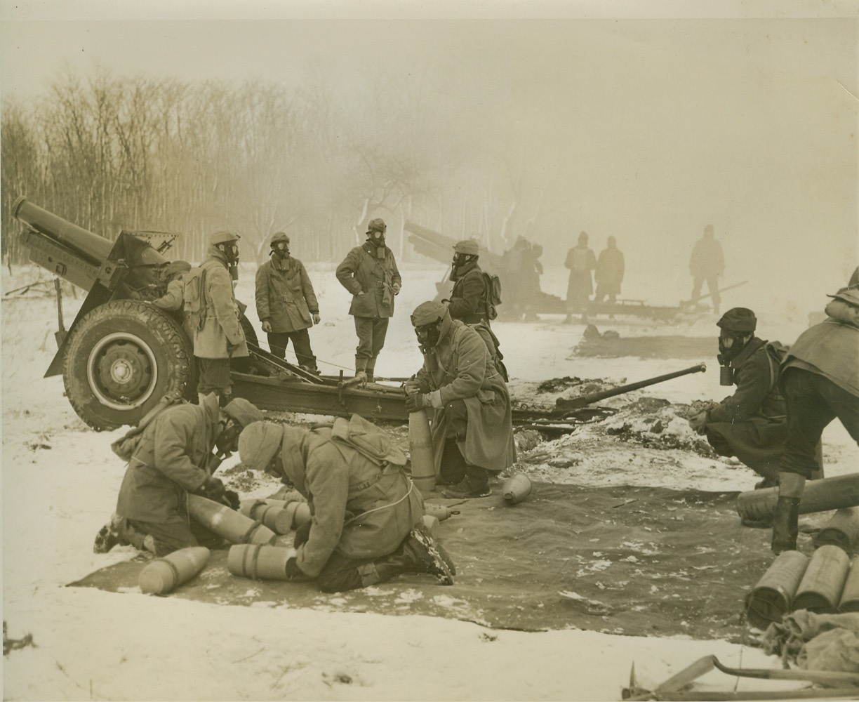 BATTERY UNDER GAS ATTACK AT FORT DIX, 1/28/41  FORT DIX, N.J. – A Battery of 155mm Howitzers of the 44th Division, under heavy gas attack from the “enemy” during maneuvers here, Jan. 28th, goes into action in a clearing in a snow-clad patch of woods. The Battery was attacked by gas by members of the 174th Infantry. Credit: OWI Radiophoto from ACME;