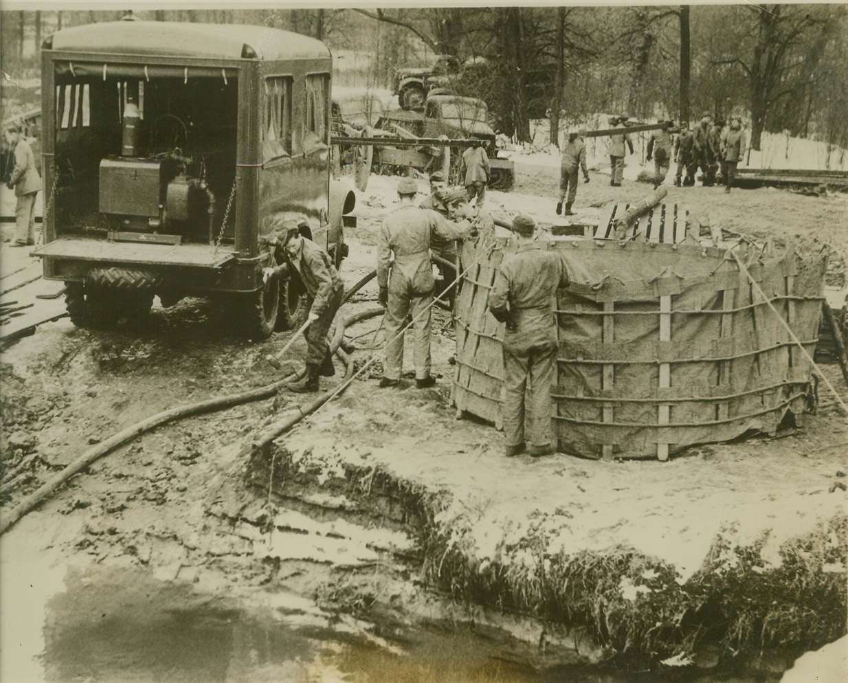 NEW MOBILE WATER PLANT, 2/1/41  FORT CUSTER, MICHIGAN- The Army is proud of this machine, a mobile water plant that pumps, purifies and delivers 150,000 gallons of water every twenty-four hours. Each unit carries four canvas 5,000-gallon tanks, one of which is shown at right of truck, and can start delivering at full capacity 30 minutes after reaching water source. Army engineers are pictured testing the machine at Fort Custer, Michigan. Credit: OWI Radiophoto from ACME;