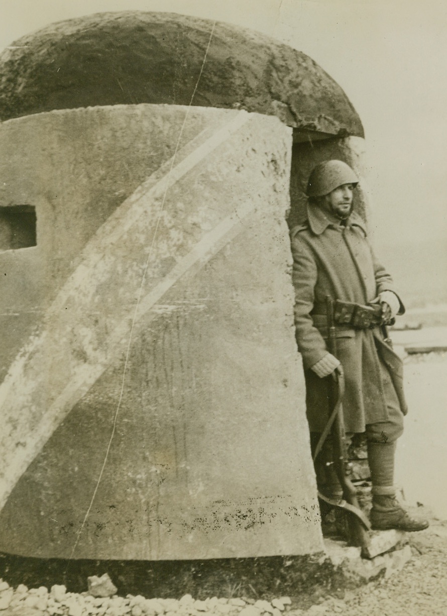 GUARDING A CAPTURED PILLBOX, 2/13/41  A Greek soldier somewhere in Albania stands guard at the door of captured pillbox that a short time ago sheltered Italian gunners. Credit: Acme;