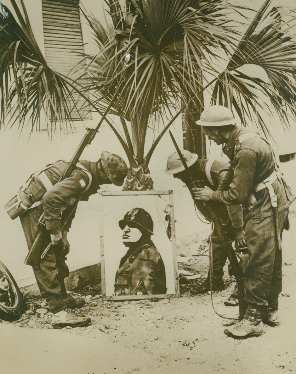 GETTING THE LAST LAUGH, 3/11/41  DERNA—These British infantrymen who participated in the capture of Derna counted this portrait of Mussolini among their prizes of war. The Tommies are getting quite a laugh from the “bull-dog” expression.;